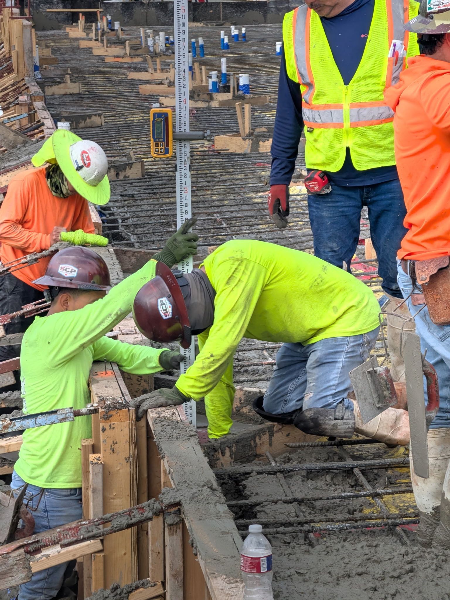 Construction workers in safety gear pouring concrete at a work site