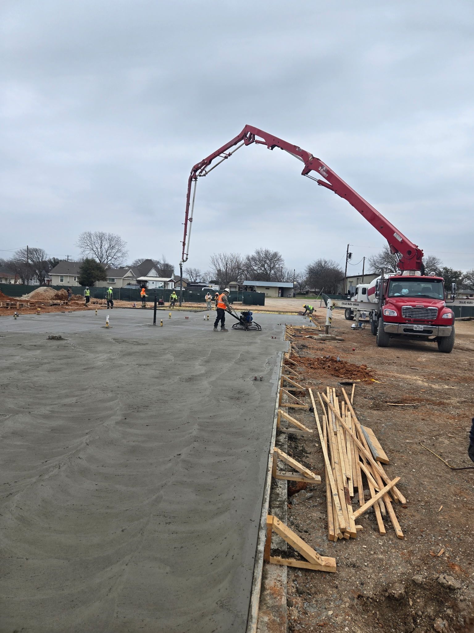 Construction site with a red concrete pump truck pouring concrete beside a fresh paved road.