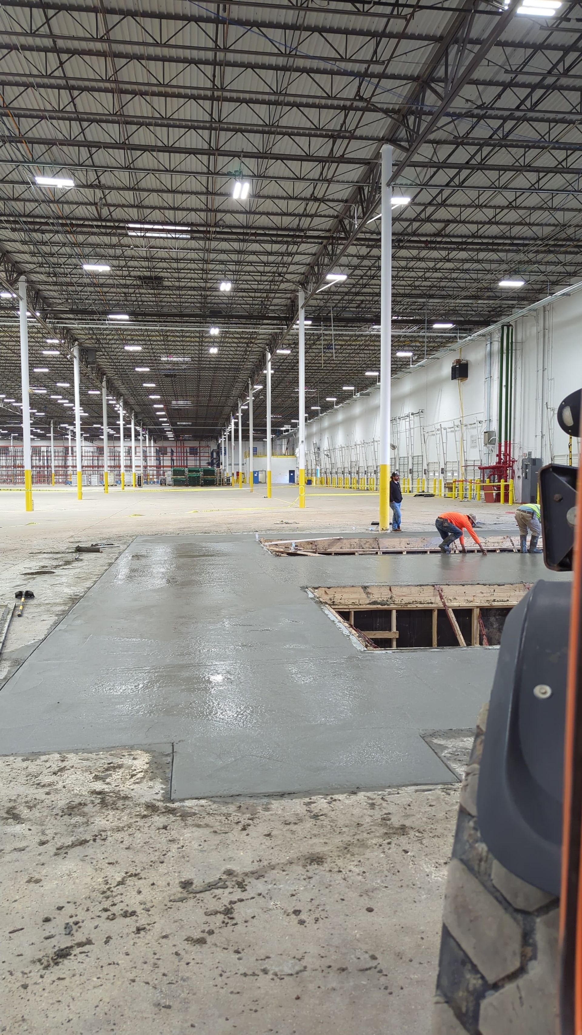 A man is working on a concrete floor in a large warehouse.
