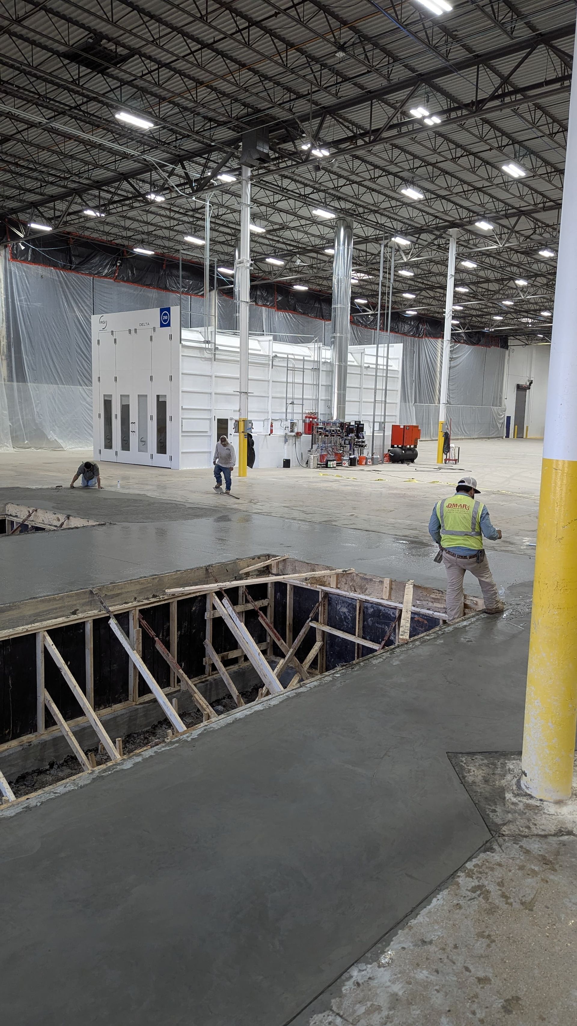 A man is working on a concrete floor in a large warehouse.