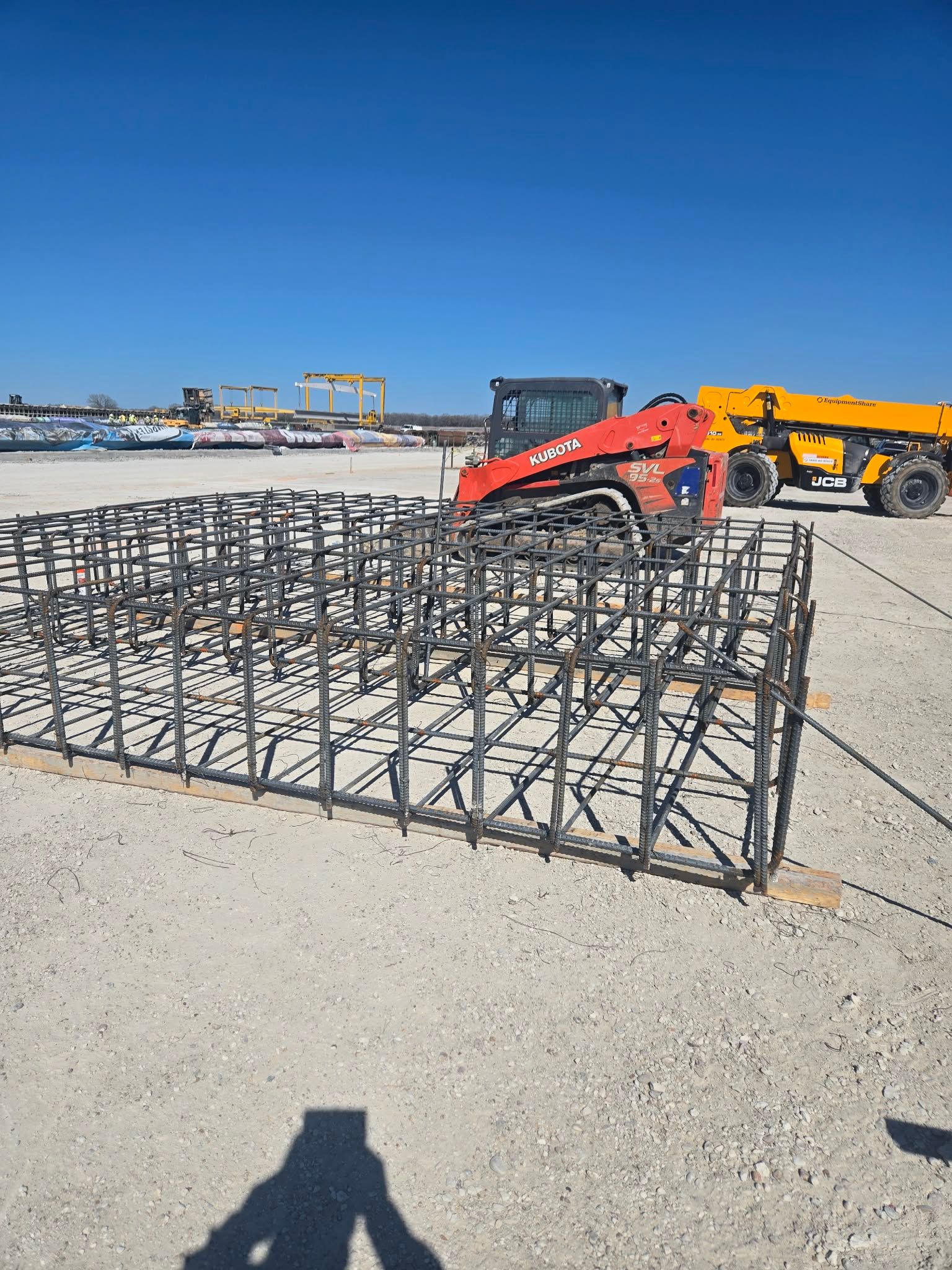 A concrete pump is being used to pour concrete on a muddy construction site.
