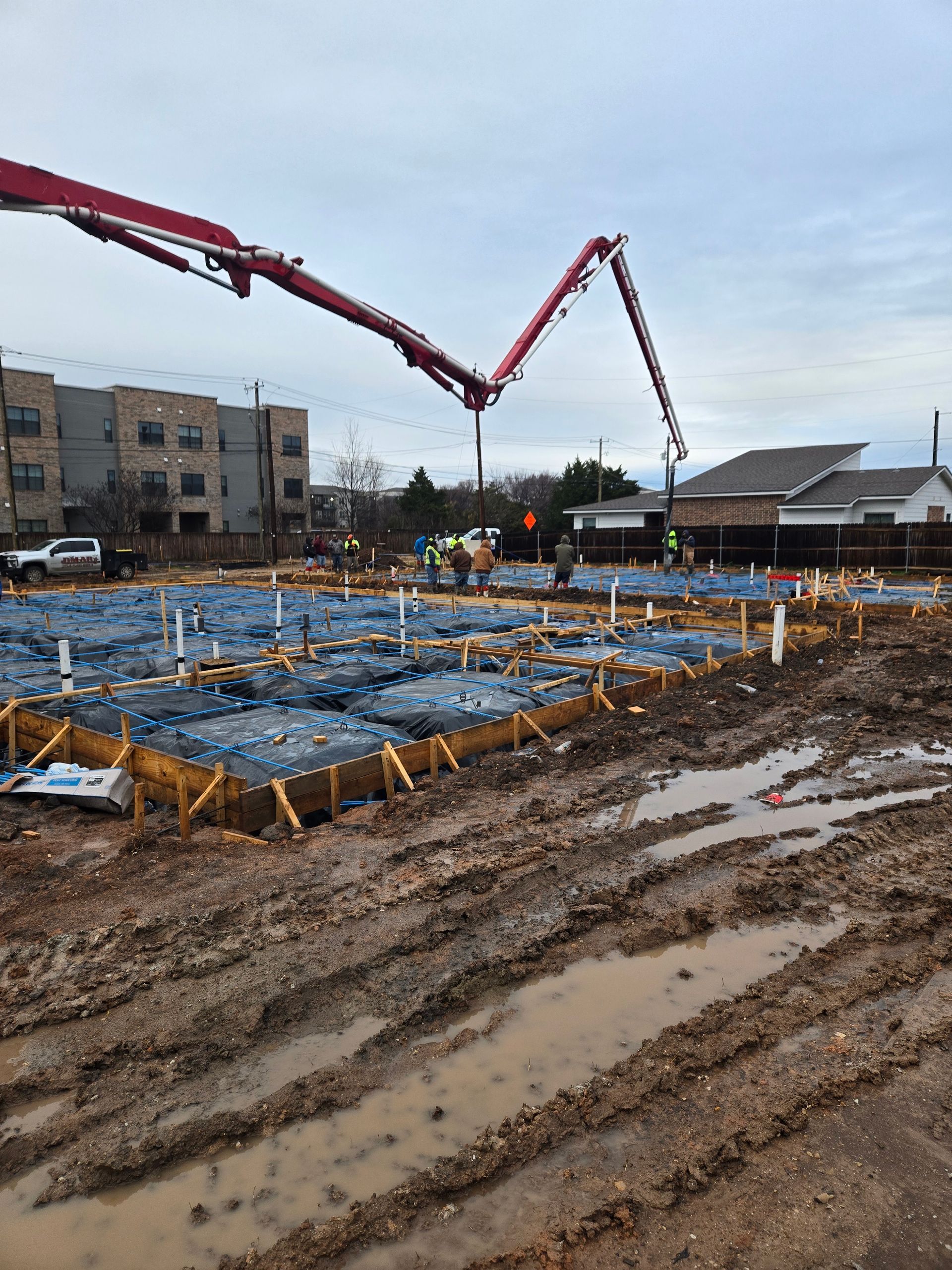 A concrete pump is being used to pour concrete on a muddy construction site.