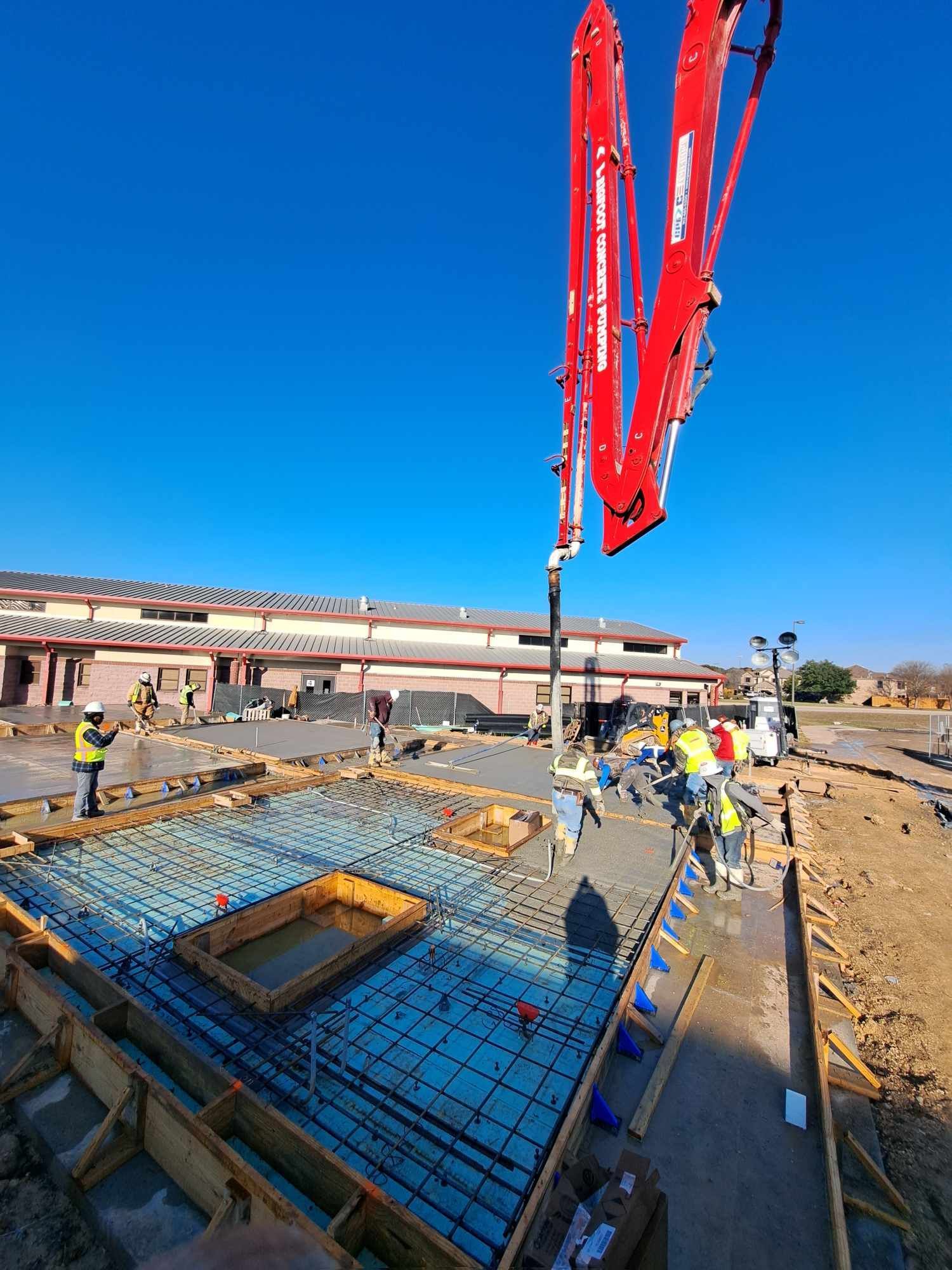 A red concrete pump is being used to pour concrete on a construction site.