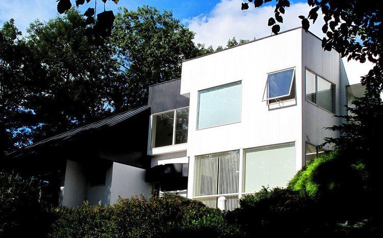 A white house with a black roof is surrounded by trees