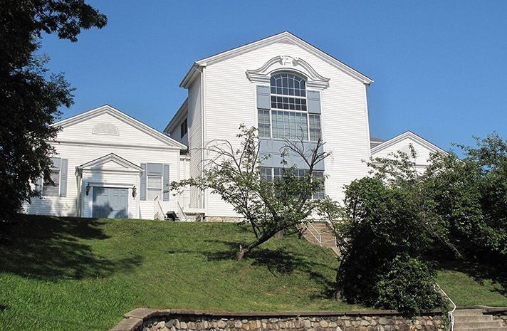 A large white house sits on top of a grassy hill