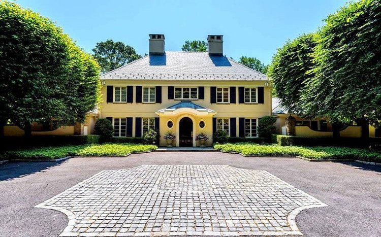 A large yellow house with black shutters is surrounded by trees