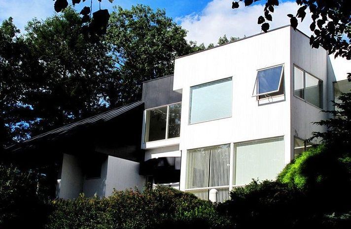 A white house with a black roof is surrounded by trees