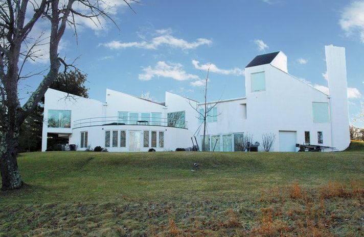 A large white house sits in the middle of a grassy field