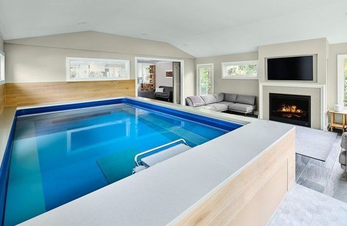 A large indoor swimming pool in a living room with a fireplace.