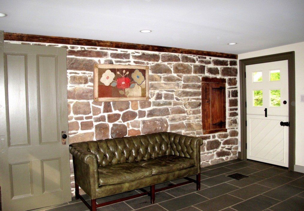 A green leather couch is sitting in front of a stone wall