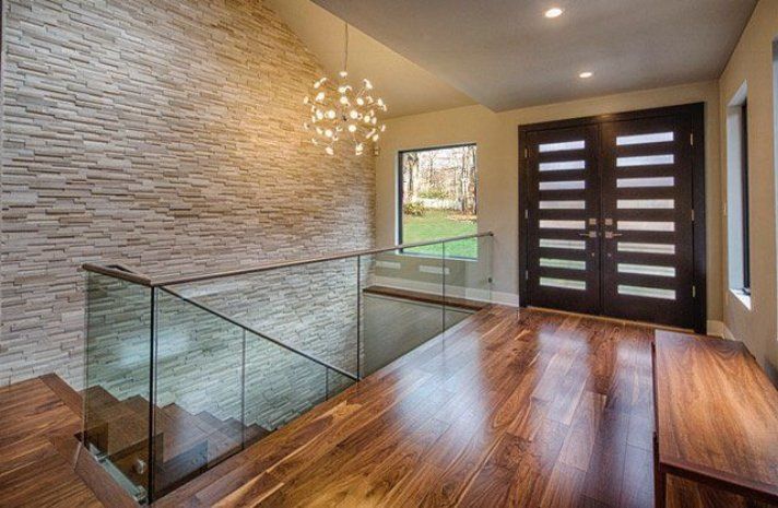 A hallway with hardwood floors and a glass railing leading to the second floor.