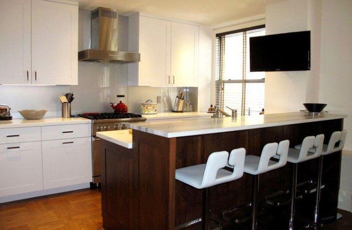 A kitchen with white cabinets and stools and a flat screen tv