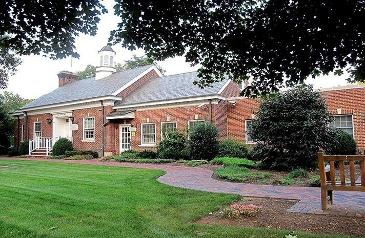 A large brick building with a blue roof sits in the middle of a lush green field