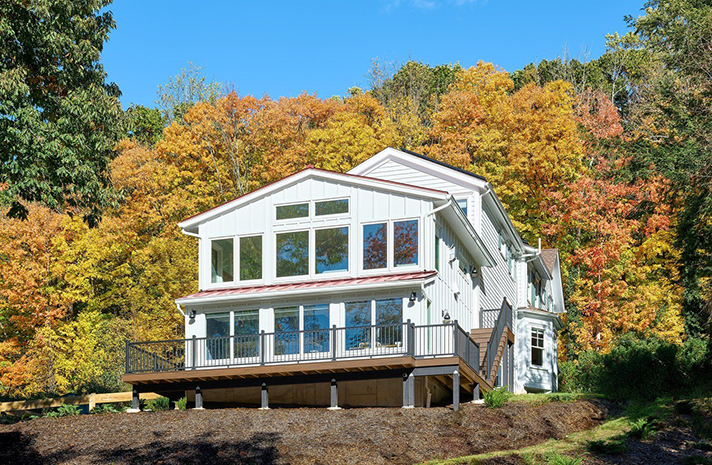 A large white house with a large deck is surrounded by trees.