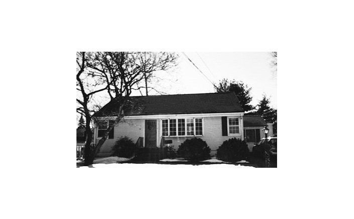 A black and white photo of a small house with a black roof