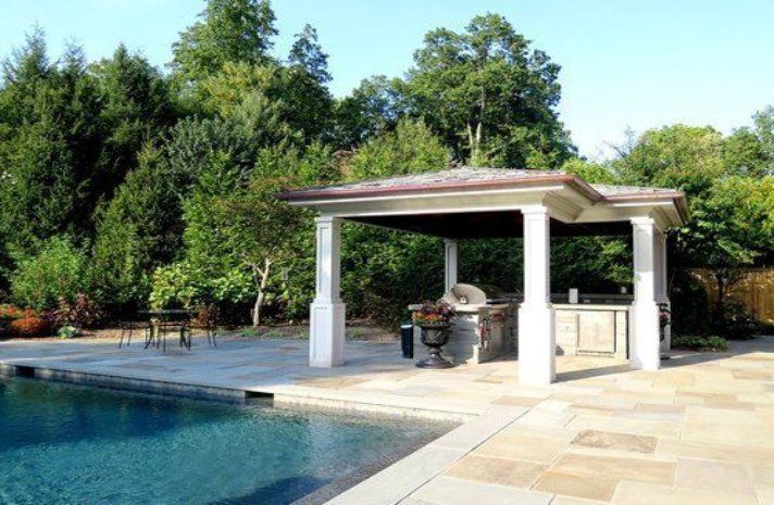 A gazebo with a grill and a swimming pool in the background.