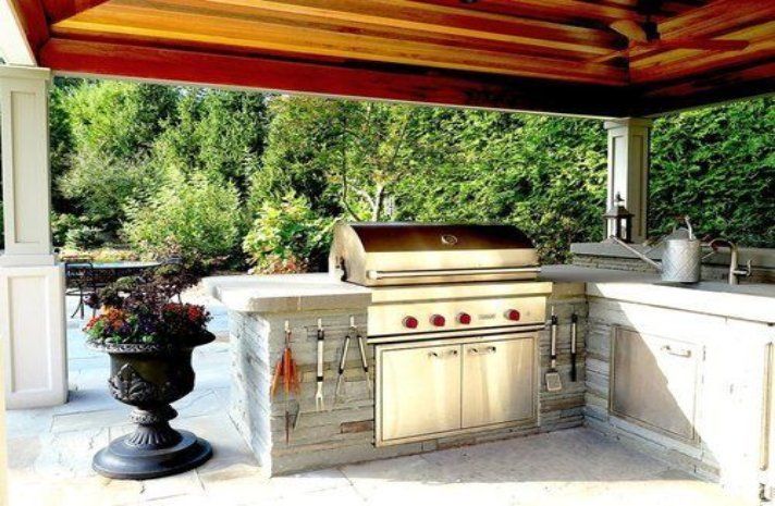 An outdoor kitchen with a grill and a sink under a wooden roof.