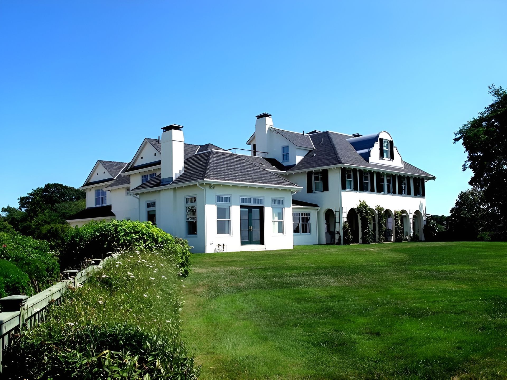 A large white house sits in the middle of a lush green field