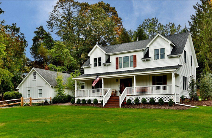 A large white house with a large porch is surrounded by trees