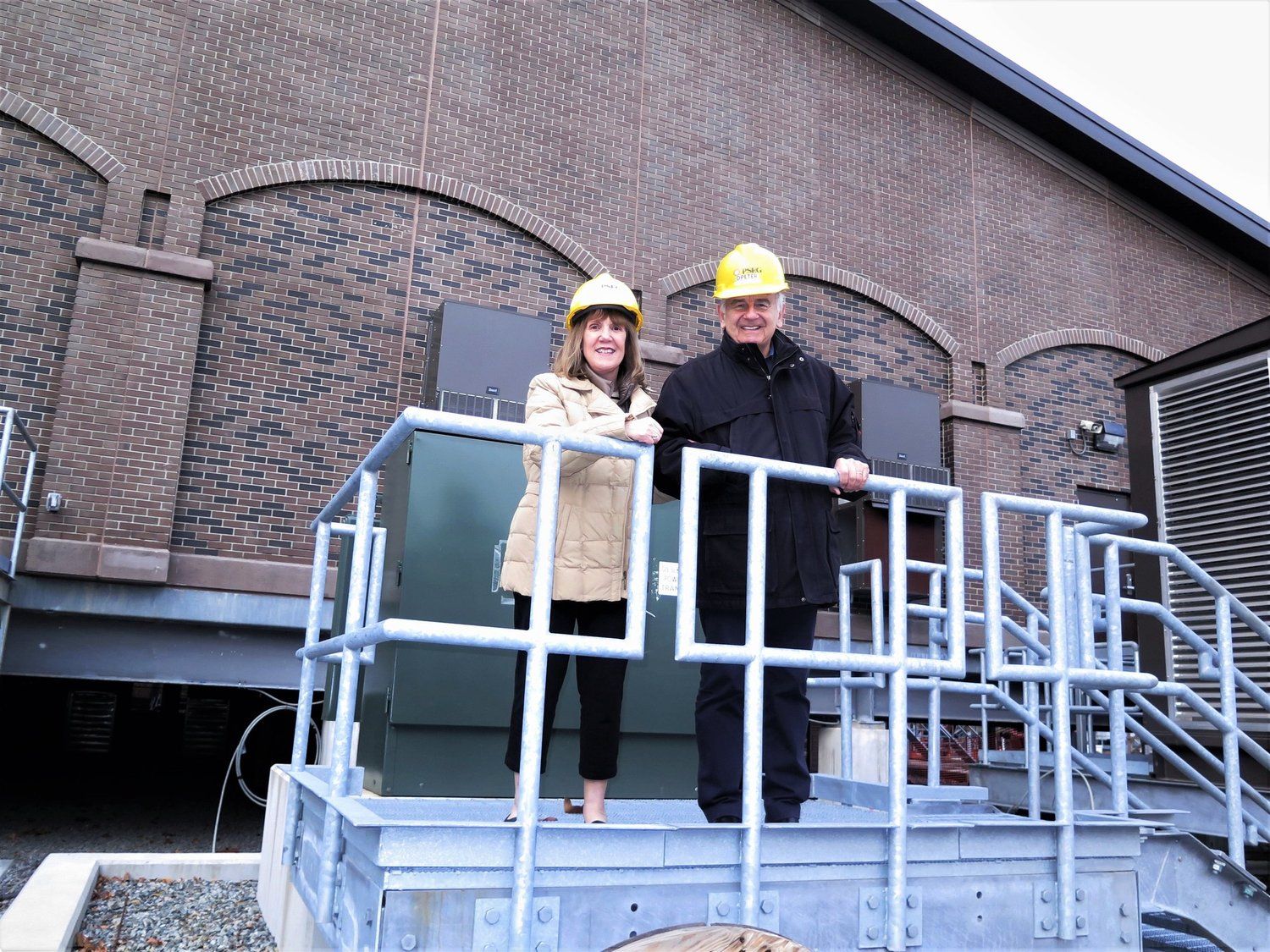 A man and a woman wearing hard hats are standing on a staircase.