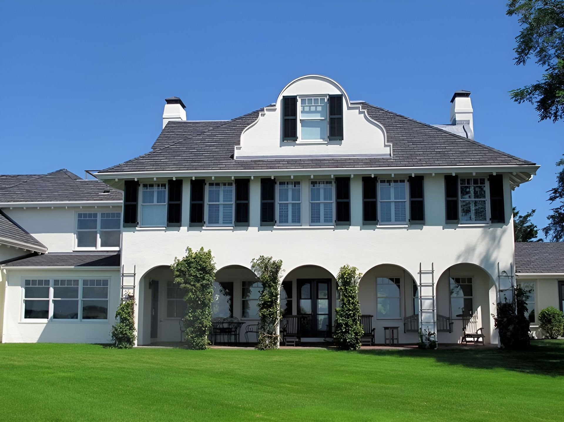 A large yellow house with black shutters is surrounded by trees