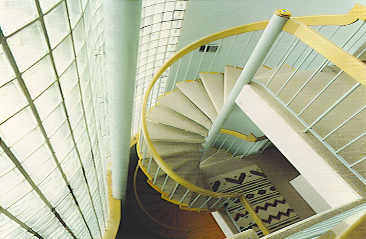 A spiral staircase with a yellow railing leading up to the second floor