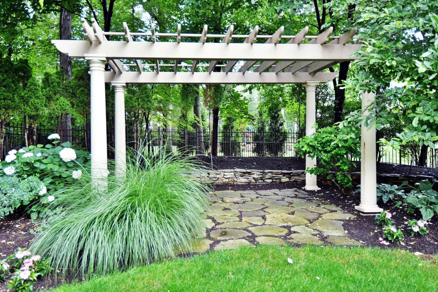 A white pergola is in the middle of a lush green garden.