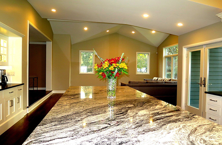 A vase of flowers sits on a granite counter in a kitchen.