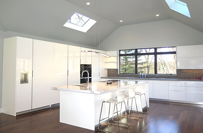 A kitchen with white cabinets , a large island , and a skylight.