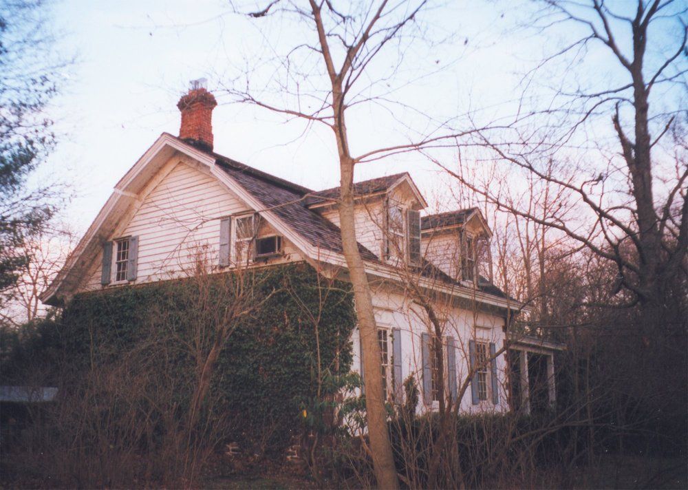 A white house with a chimney on the roof is surrounded by trees