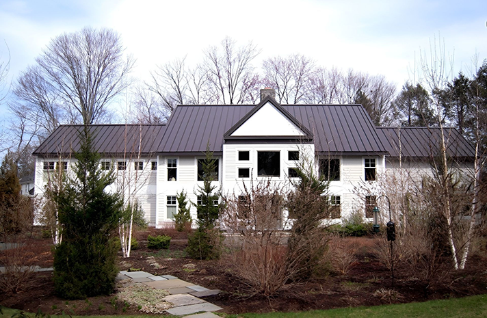 A large white house with a black roof is surrounded by trees and bushes.