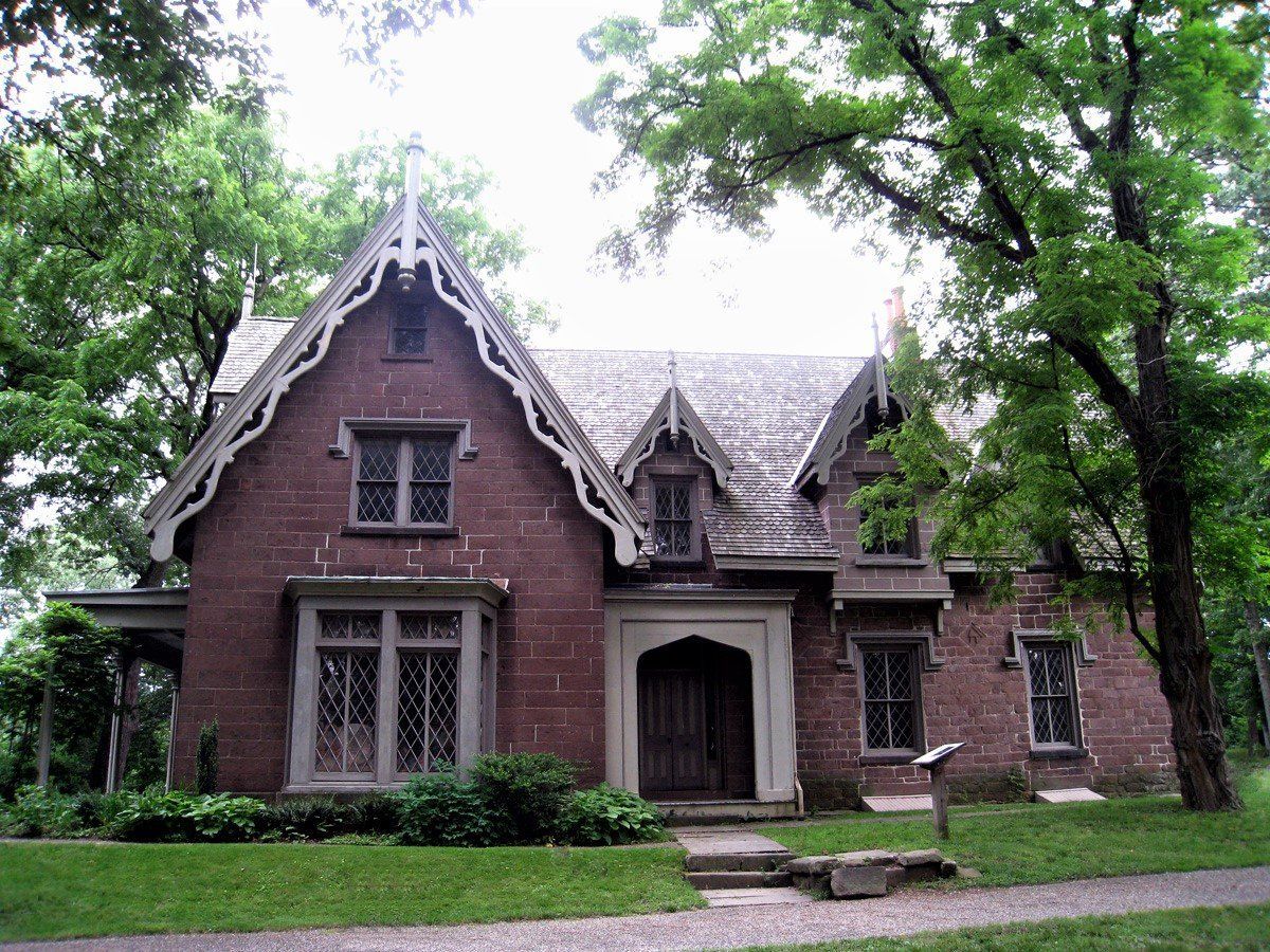 A brick house with a pointed roof is surrounded by trees