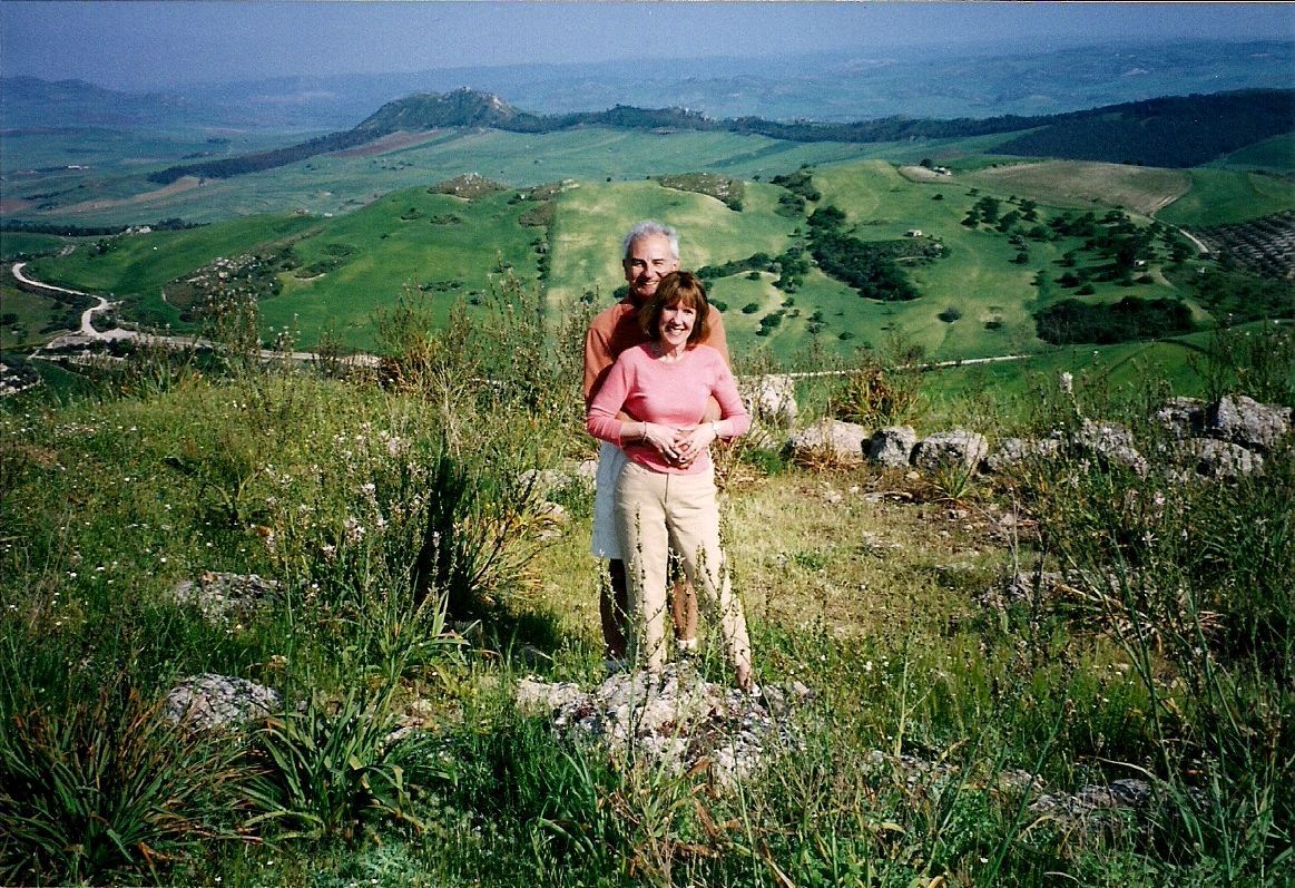 A man and woman standing on top of a grassy hill