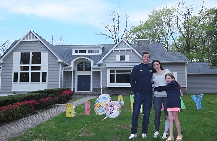 A family is standing in front of a house holding balloons.