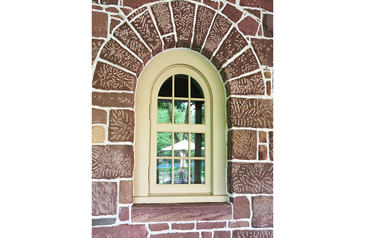 An arched window on a brick wall with a pool in the background