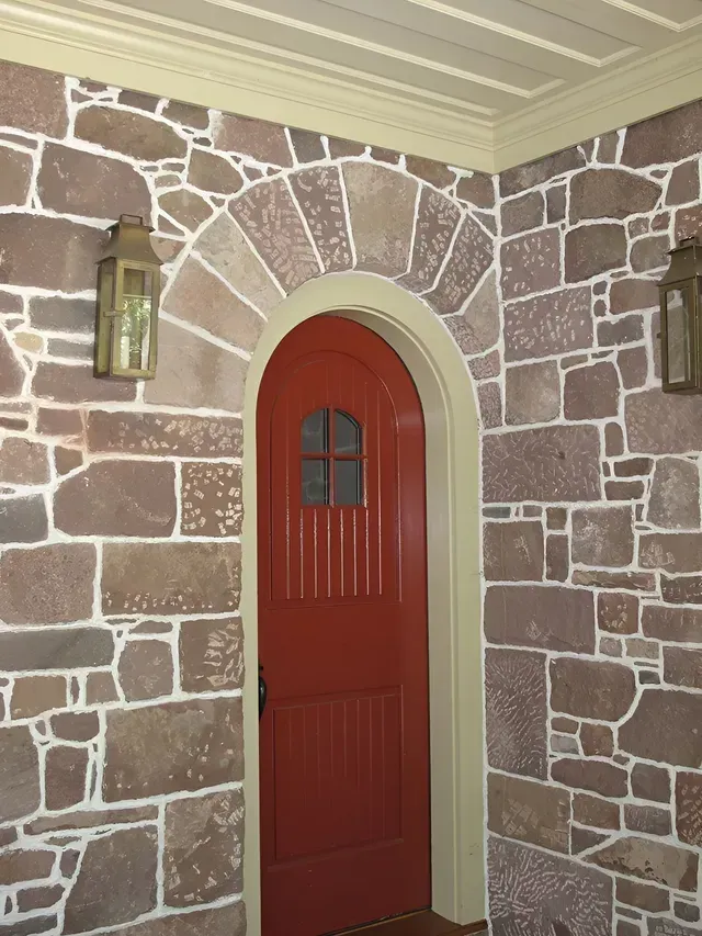 A stone wall with a red door and two lanterns