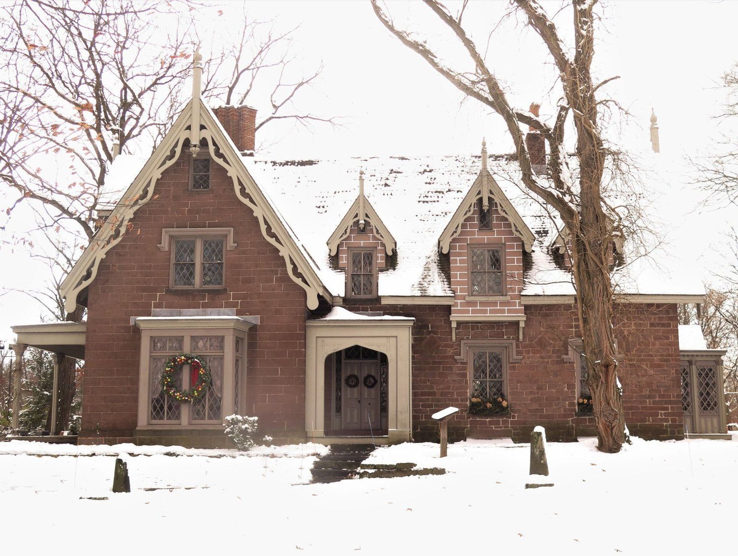 A brick house is covered in snow and has a wreath on the front door.