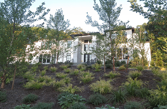 A large white house is surrounded by trees and bushes