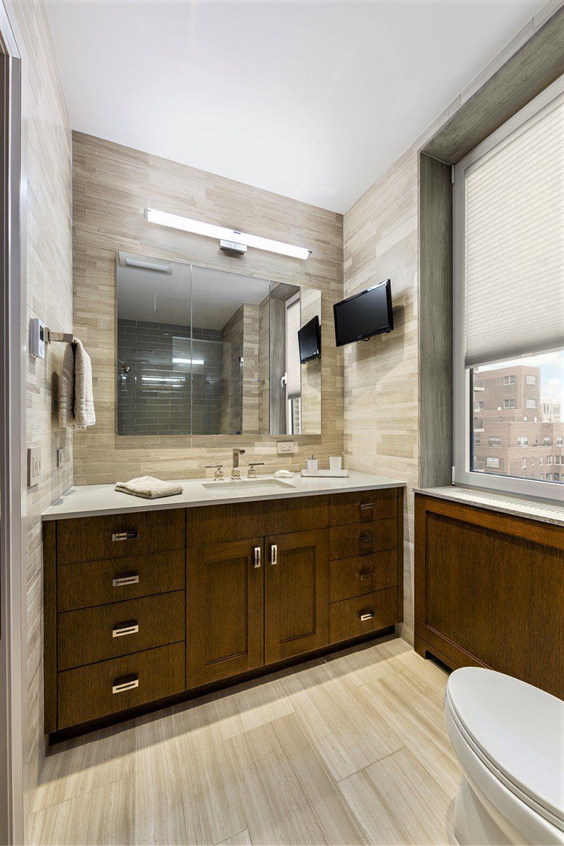 A bathroom with a toilet , sink , mirror and television.