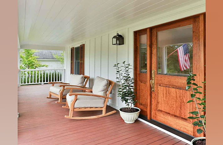 There are two rocking chairs on the porch of a house.
