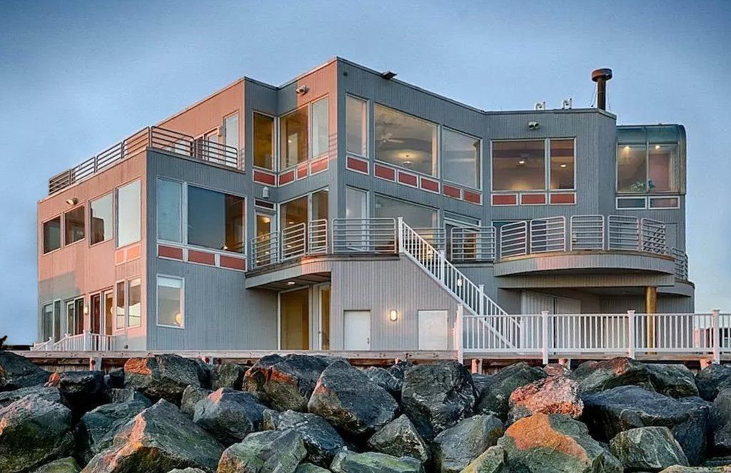 A large house is sitting on top of a rocky shoreline.