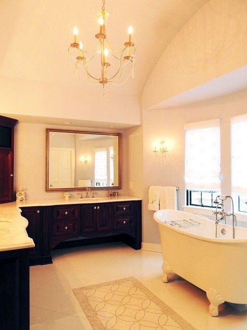A bathroom with a tub , sink , mirror and chandelier