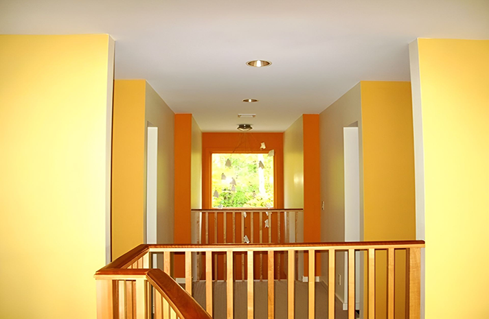 A hallway with yellow and orange walls and a wooden railing