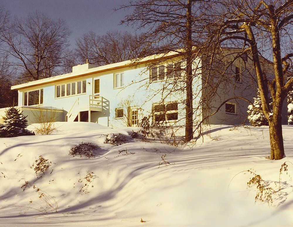 A blue house is surrounded by snow and trees