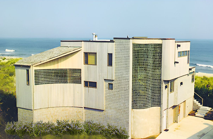 A large white house sits on top of a hill overlooking the ocean