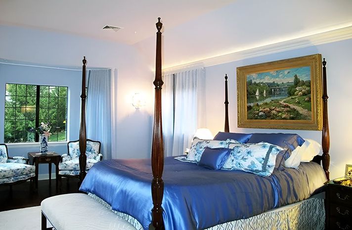 A bedroom with a four poster bed and a painting on the wall