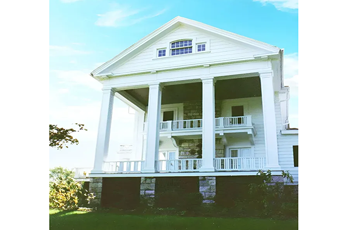 A large white house with columns and balconies on a sunny day.