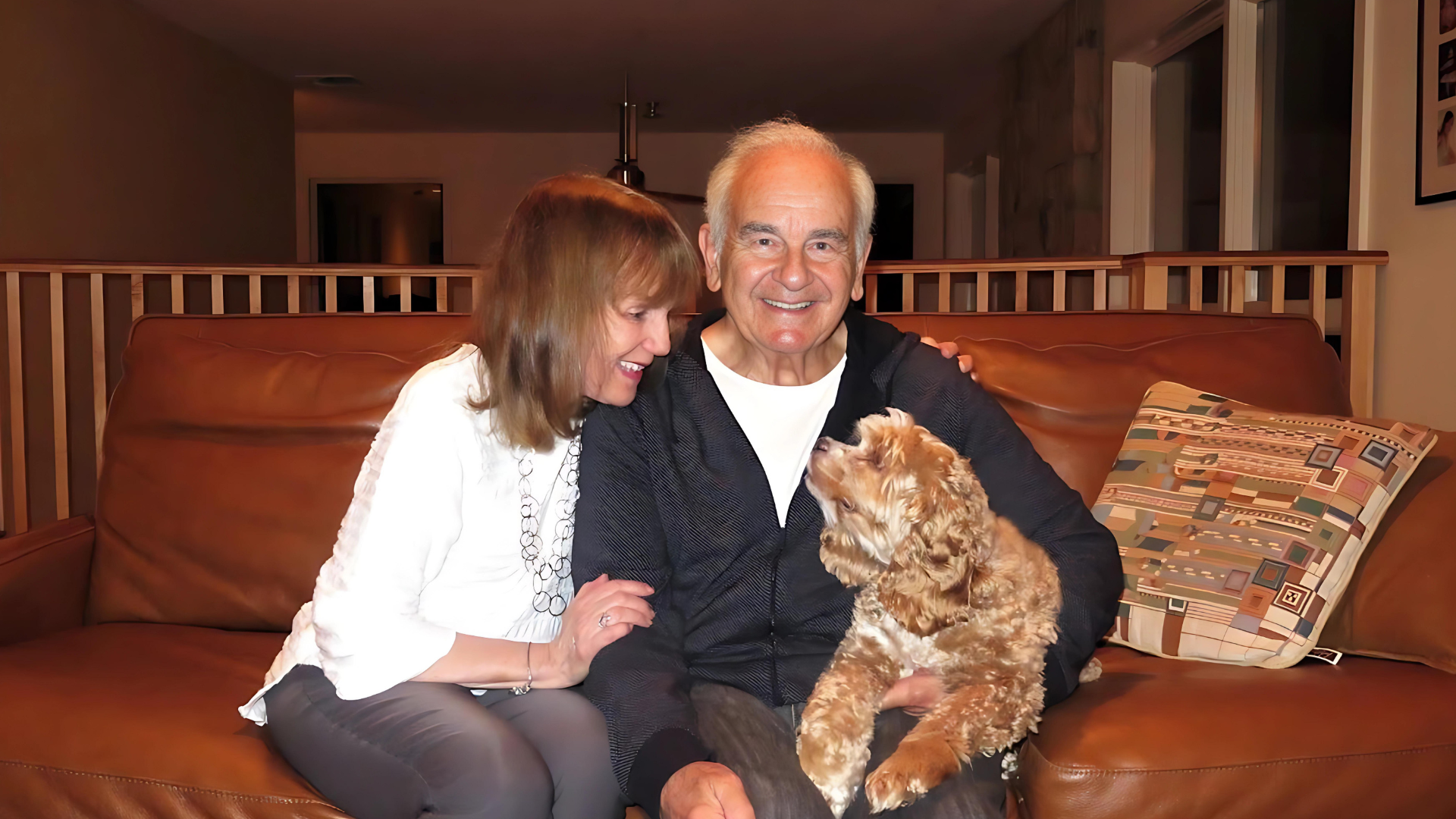 A man and a woman are sitting on a couch holding a dog