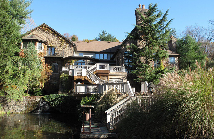 A large house is surrounded by trees and a body of water