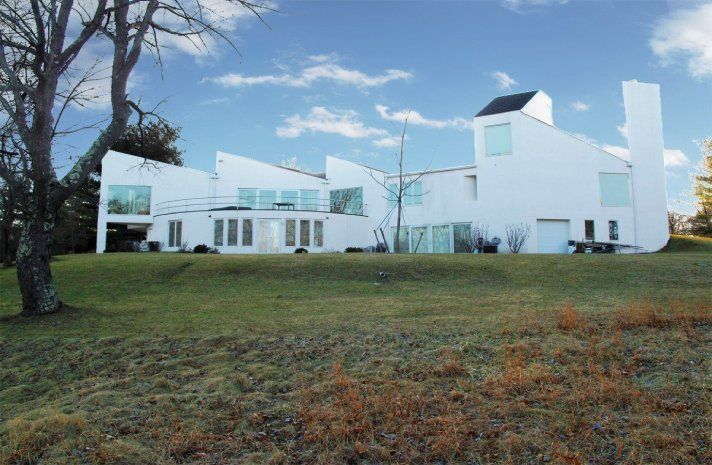 A large white house sits in the middle of a grassy field